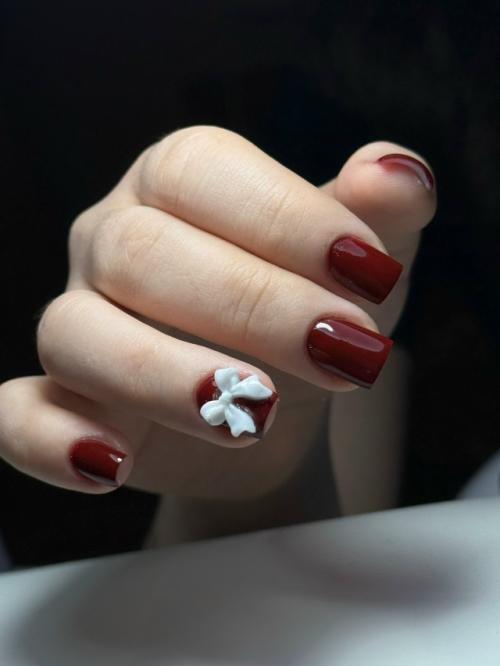 Элегантный бордовый маникюр с изящным белым бантиком на одном из ногтей - сочетание классики и игривости!  